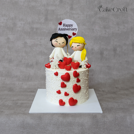 Anniversary couple cake with ivory white base, red fondant hearts, and cute couple toppers by CakeCroft Dhaka.