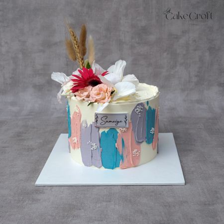 Ivory buttercream cake with pastel blue, peach, and lilac brushstrokes, topped with fresh flowers and wheat accents by CakeCroft Dhaka.