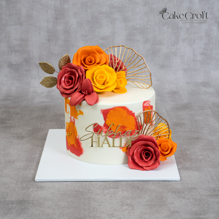 Haldi theme ivory cake with handcrafted yellow, orange, and red sugar roses, gold accents, and custom topper by CakeCroft Dhaka.