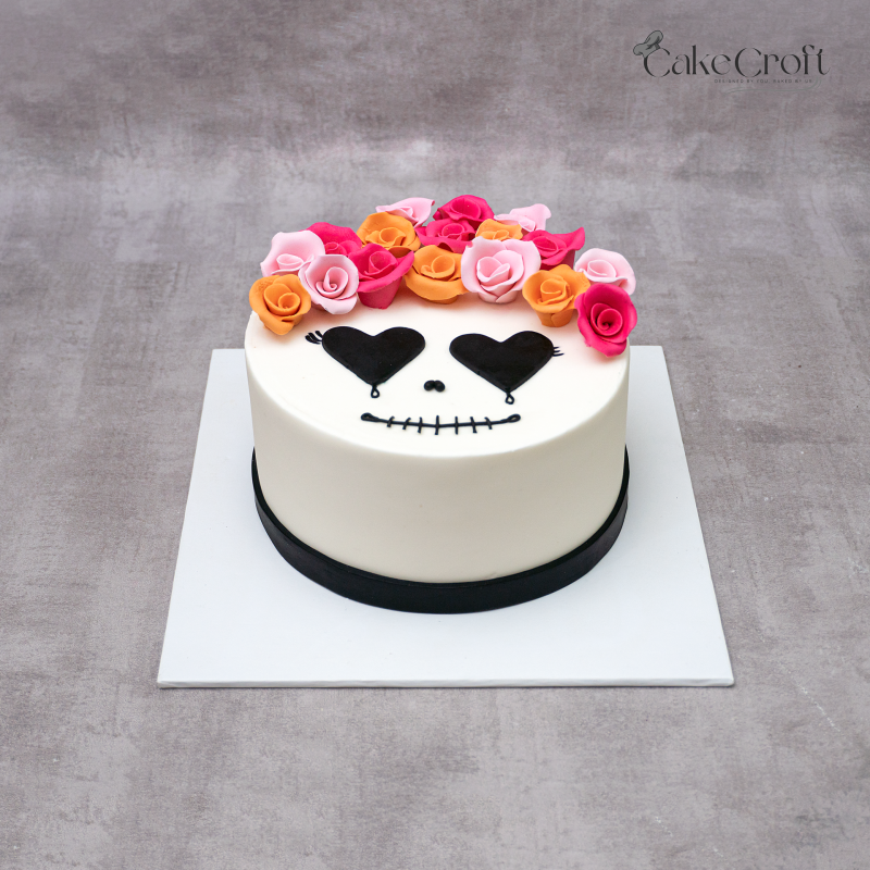 Day of the Dead cake with fondant skull face, black heart eyes, and colorful rose crown in pink, orange, and peach by CakeCroft Dhaka.