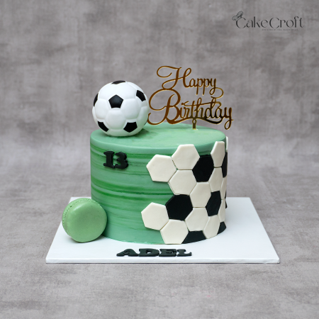 Football theme birthday cake in green marble fondant with 3D soccer ball topper, gold “Happy Birthday” sign, and black-white hexagon design by CakeCroft Dhaka.
