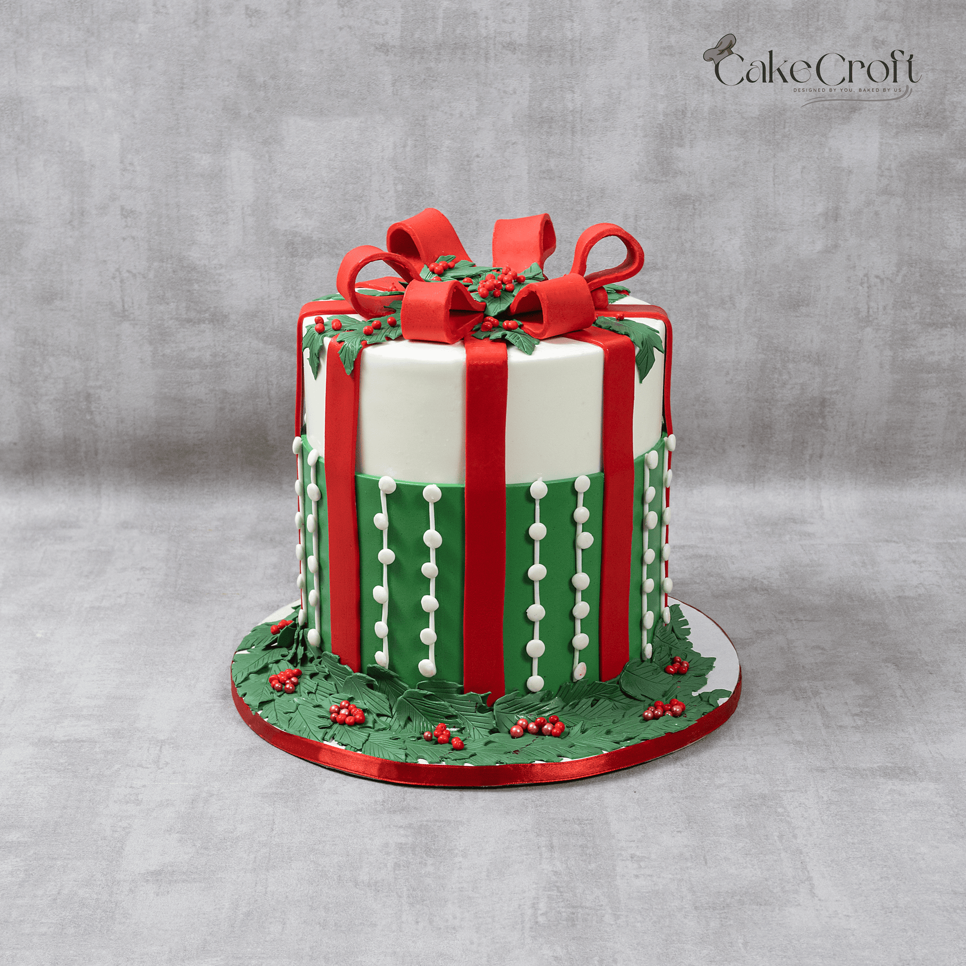Christmas gift box cake with red ribbon bow and green festive decorations.