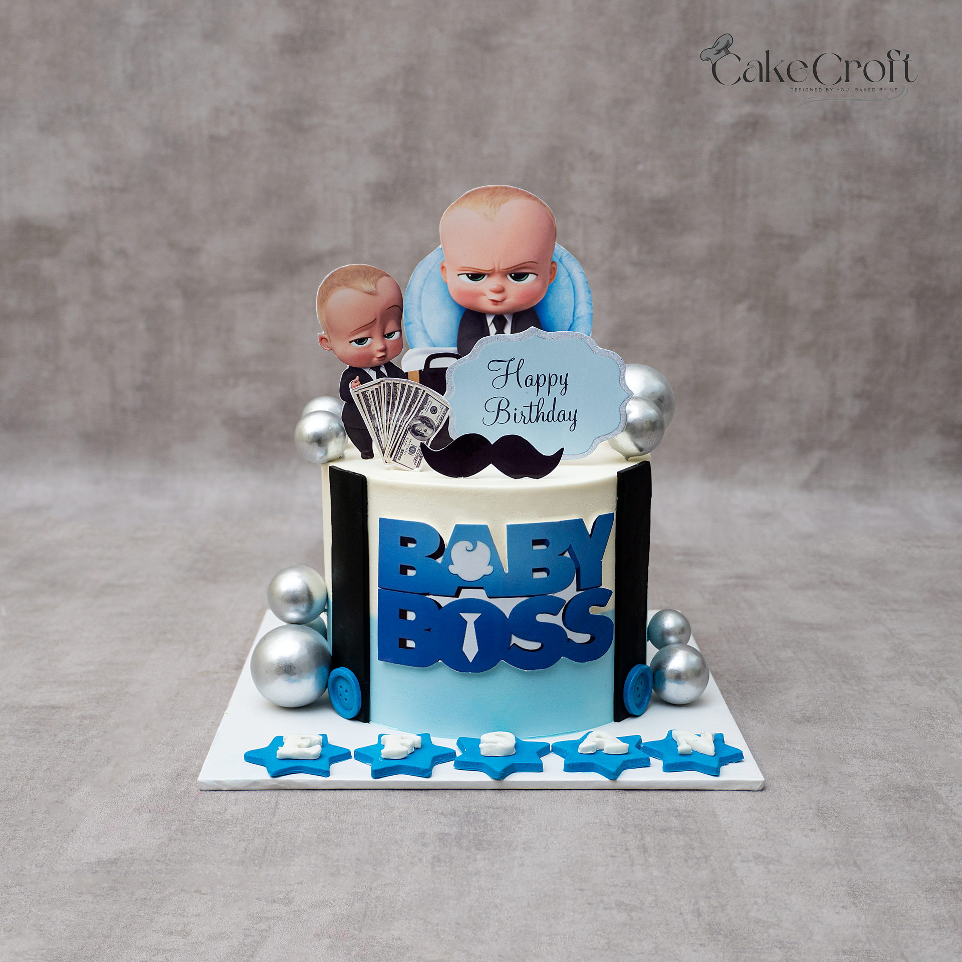 Baby Boss themed birthday cake with blue gradient design, Baby Boss character toppers, silver balls, and “BABY BOSS” fondant lettering.