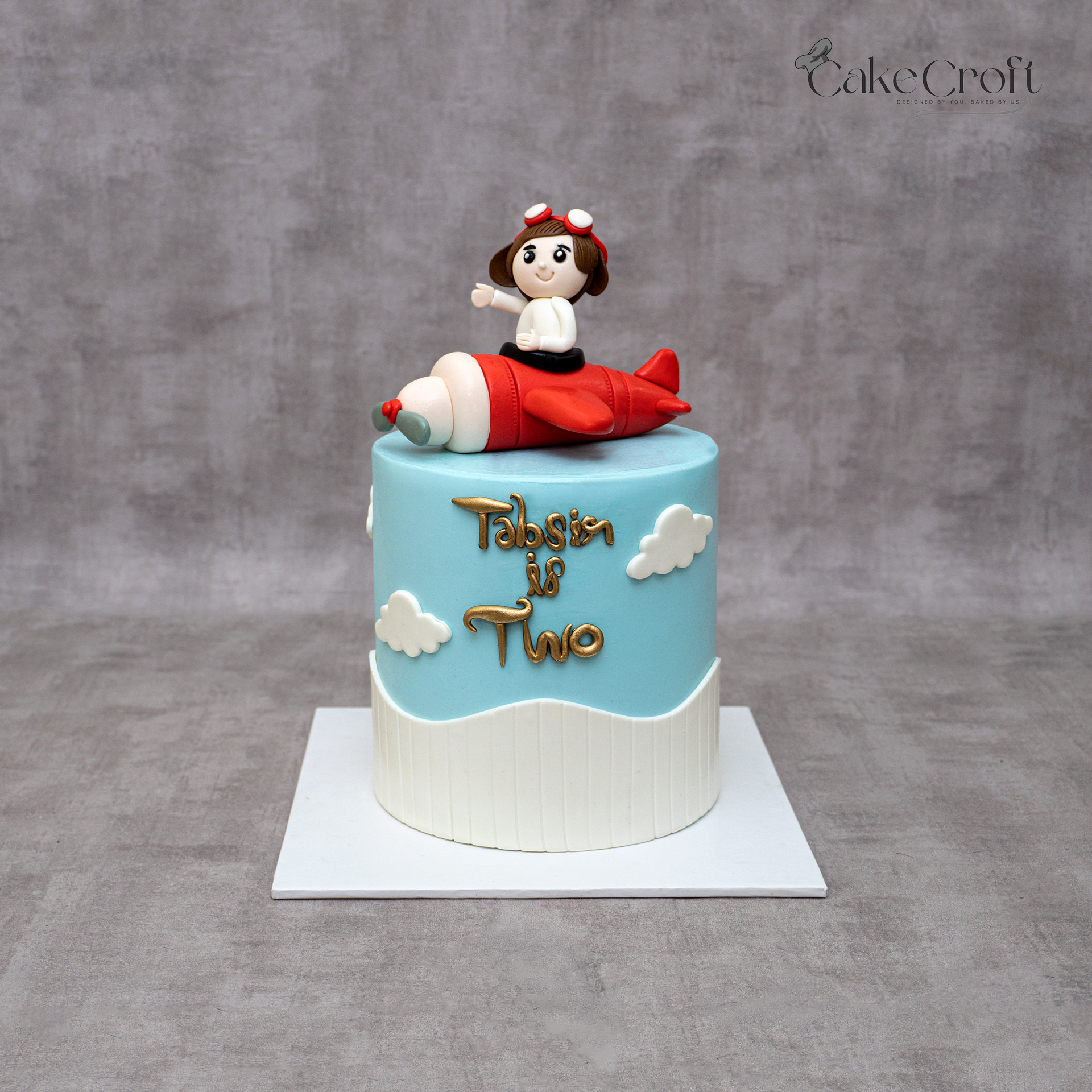 Sky-blue kids airplane cake with a fondant pilot on a red airplane and cloud decorations.