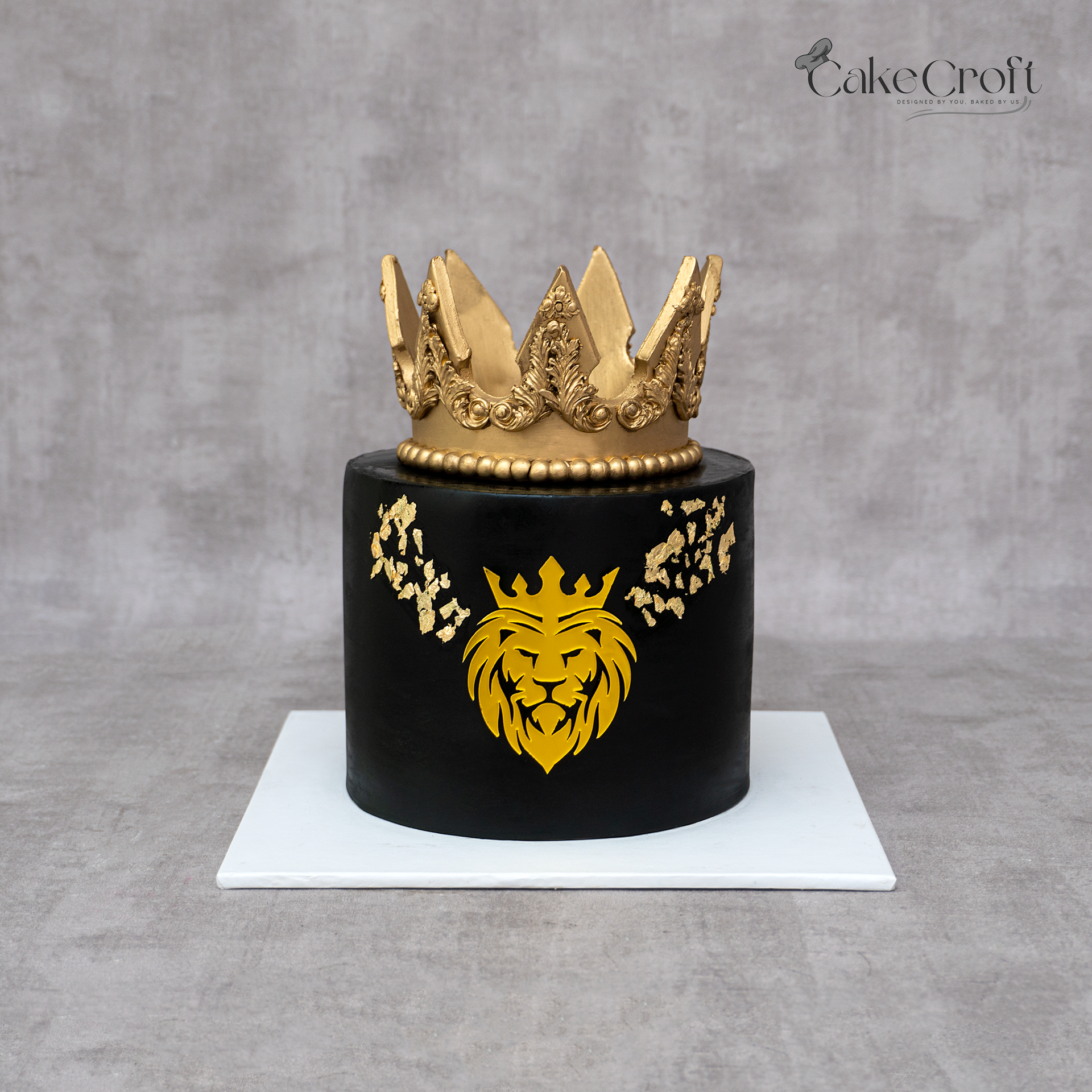 Royal black and gold crown cake with lion emblem and gold leaf detailing.