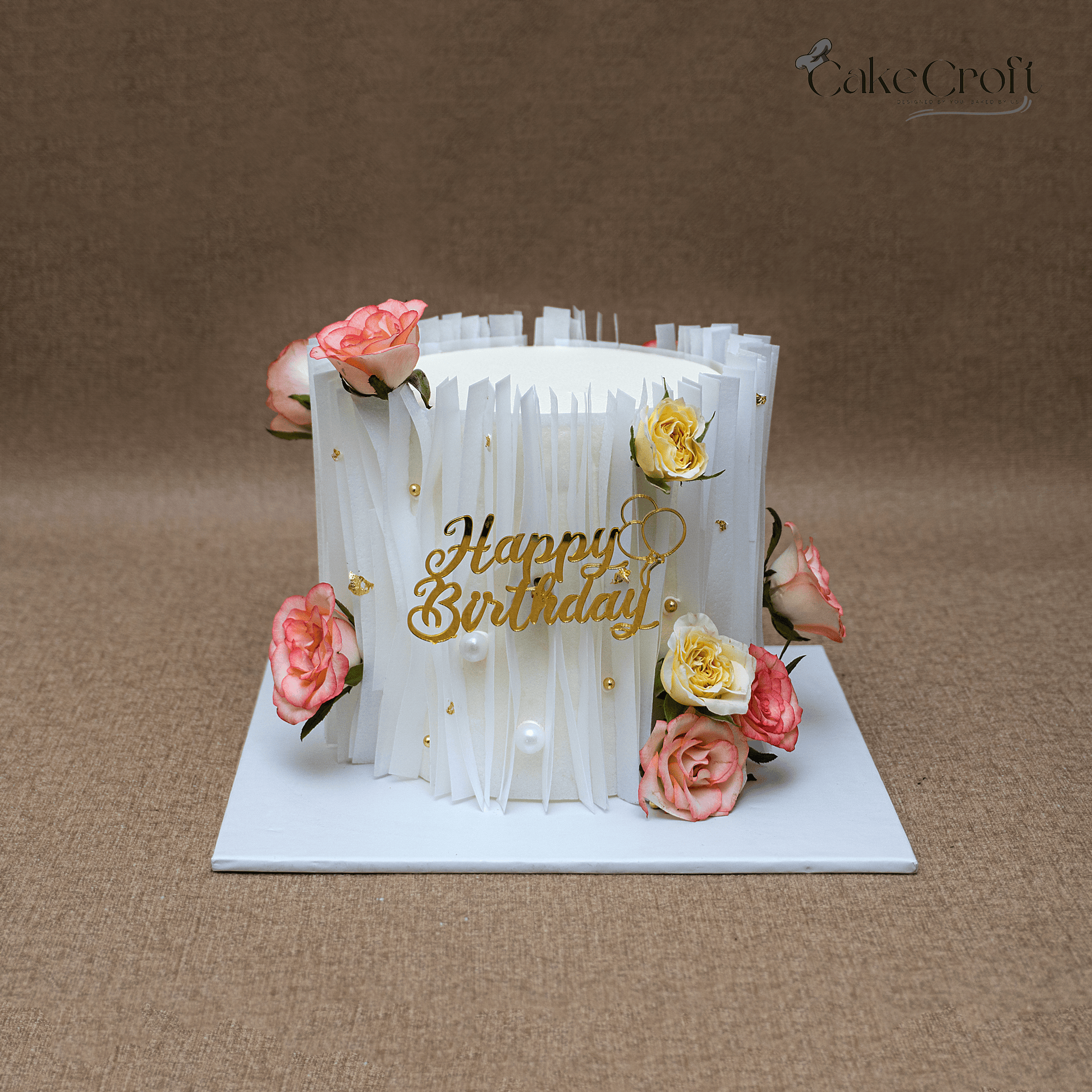 Elegant ivory floral birthday cake with roses, pearl accents, and gold Happy Birthday topper.