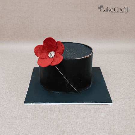 Minimalist black buttercream cake with red flower and gold detailing.