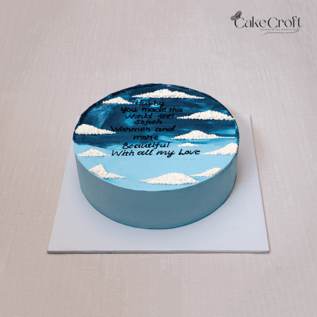 Sky blue buttercream cake with white clouds and handwritten love message.