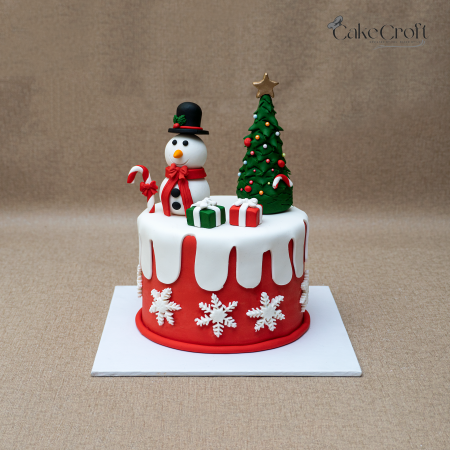 Christmas snowman cake with Christmas tree, gift boxes, and festive decorations.
