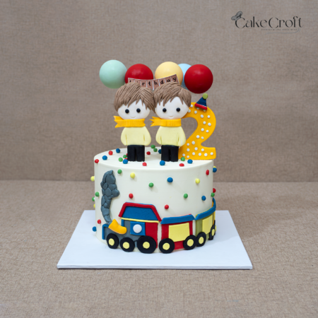 Twin birthday train cake with two figurines, balloons, and number two topper.